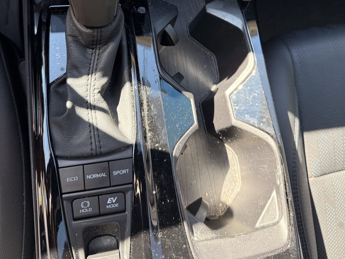 Camry center console before detailing: crumbs and dust across the gloss-black trim and inside the cupholders