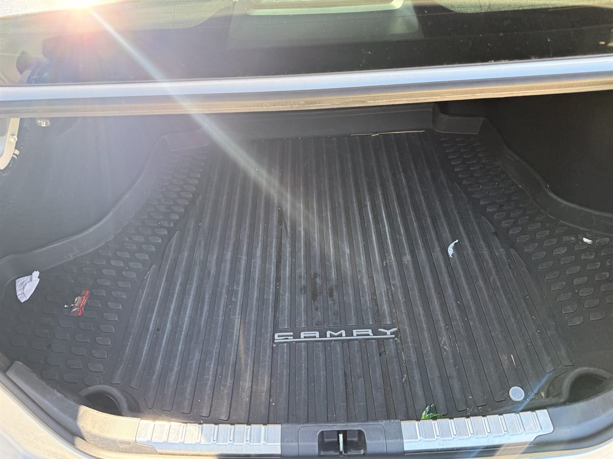 Camry trunk before detailing: dusty rubber trunk mat with a crumpled receipt, a candy wrapper and other litter